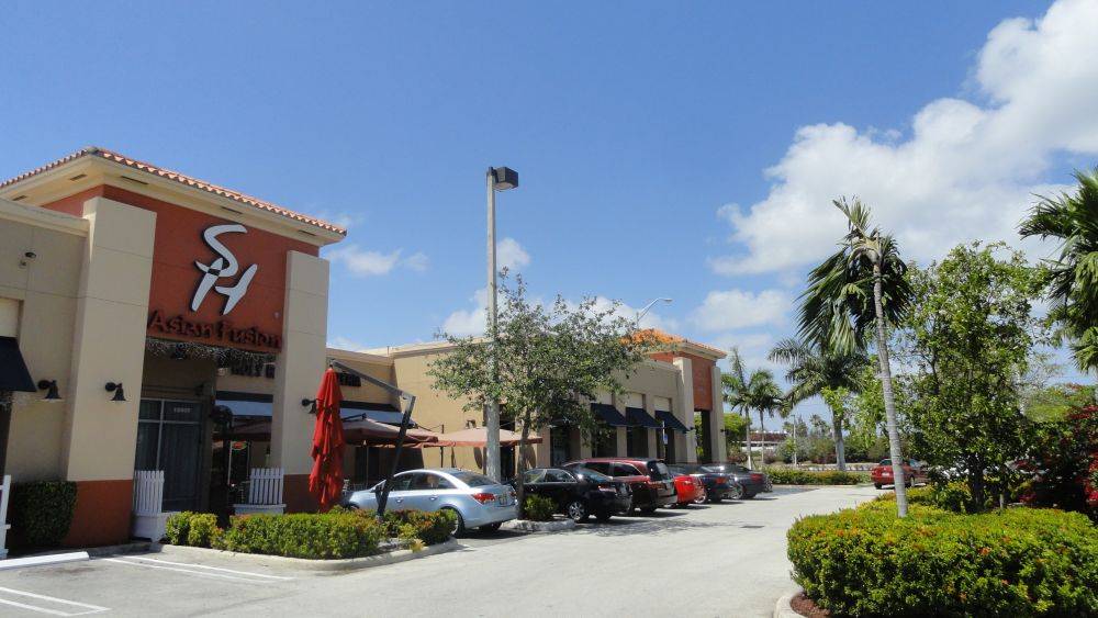 Shopping plaza with cars parked in front on a sunny day.