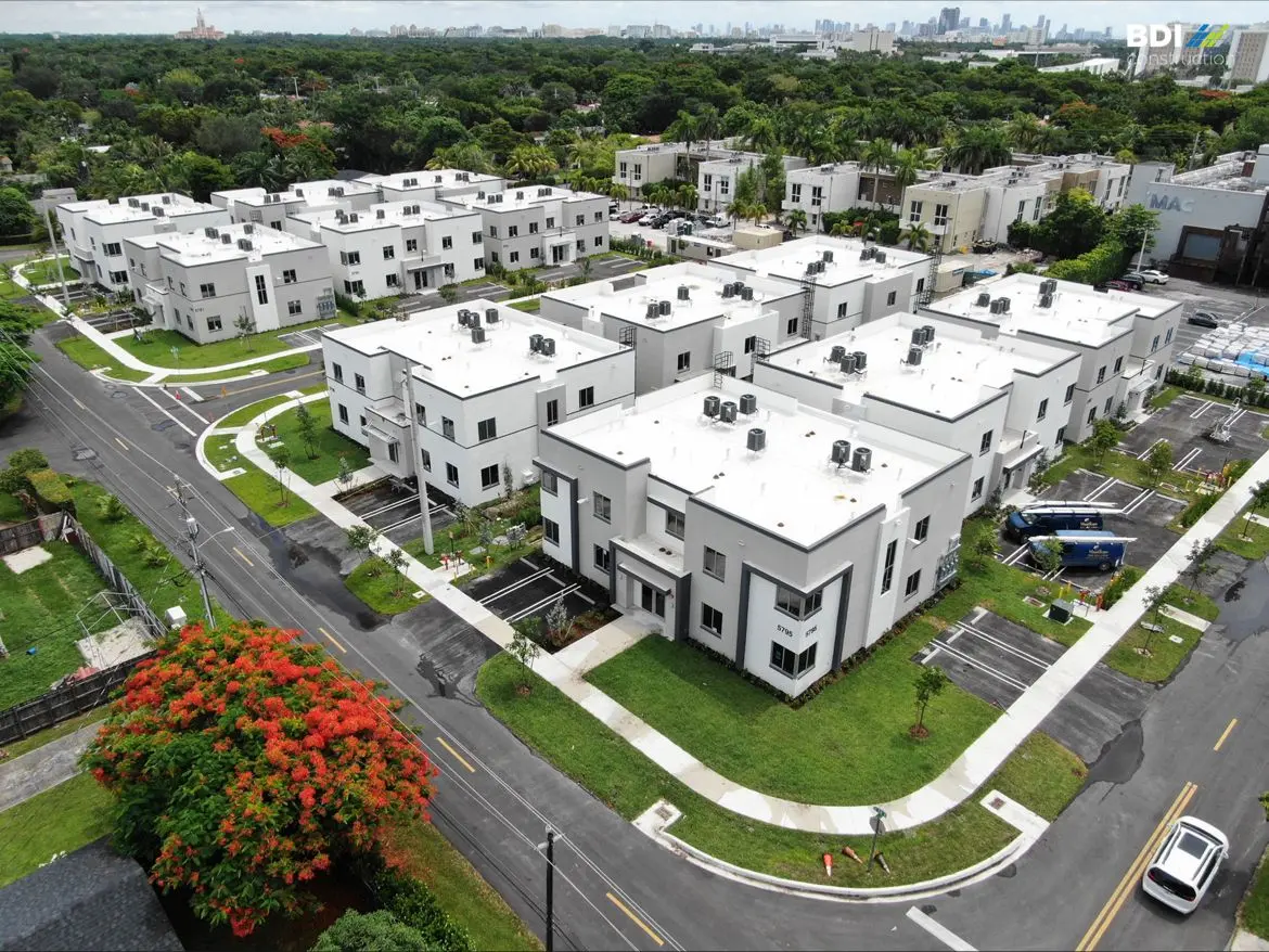 Aerial view of a modern residential neighborhood with white homes and lush greenery.