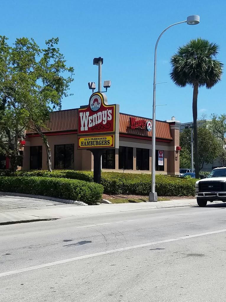 Wendy's restaurant with classic logo on a sunny day, surrounded by lush greenery and palm trees.