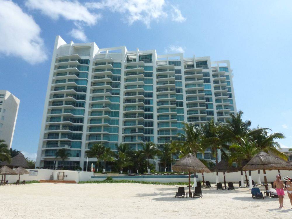 Modern beachfront condominium with palm trees and loungers under a clear blue sky.