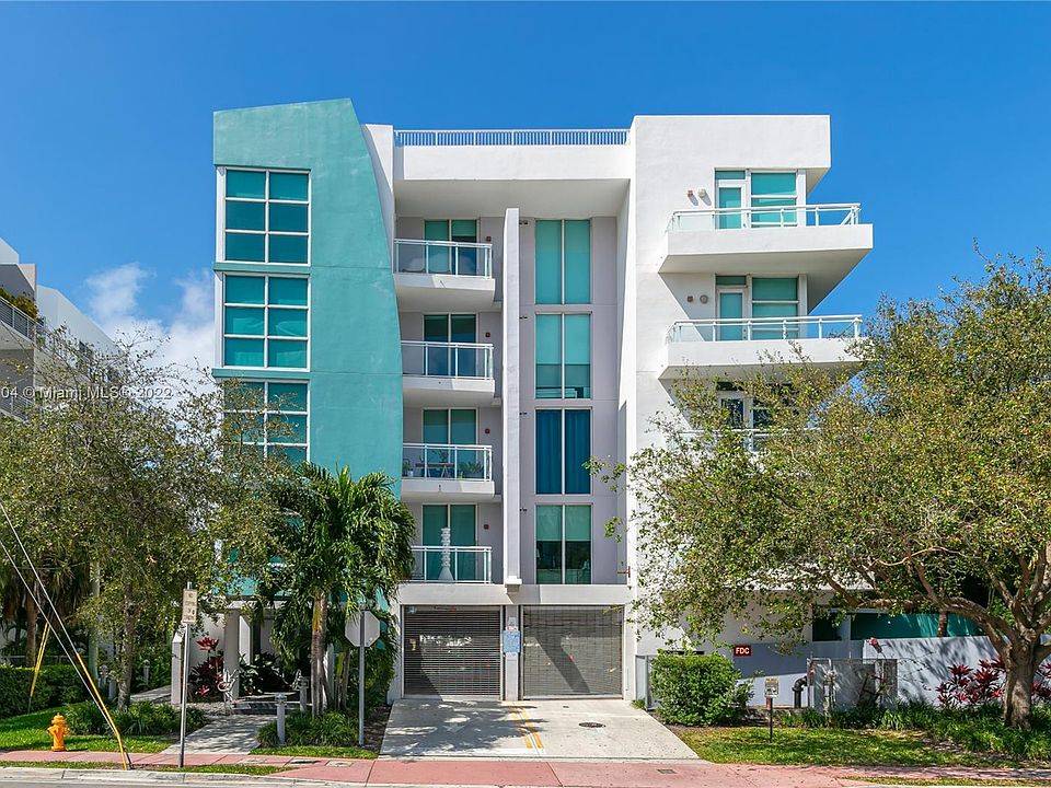 Modern white and turquoise apartment building with balconies and lush greenery.