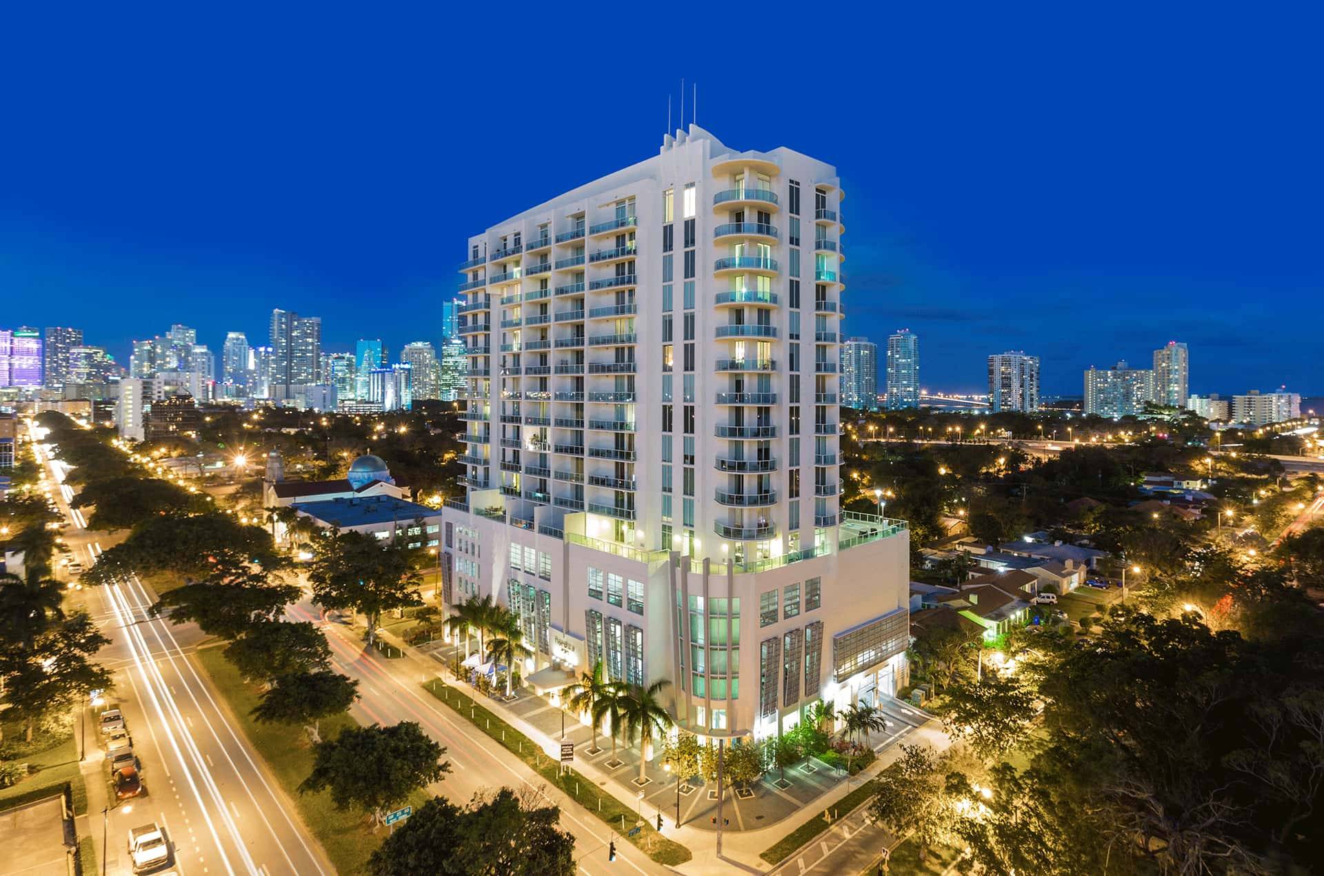 Night view of an illuminated modern high-rise building amid a vibrant cityscape.