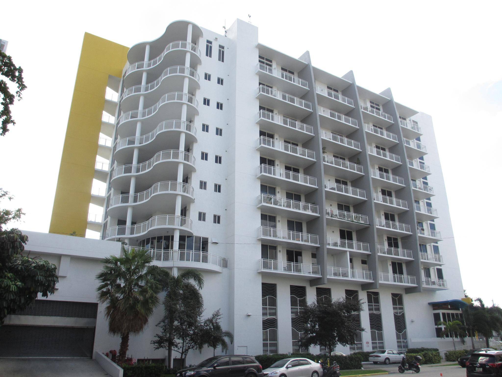 Modern white apartment building with balconies and a yellow side panel.