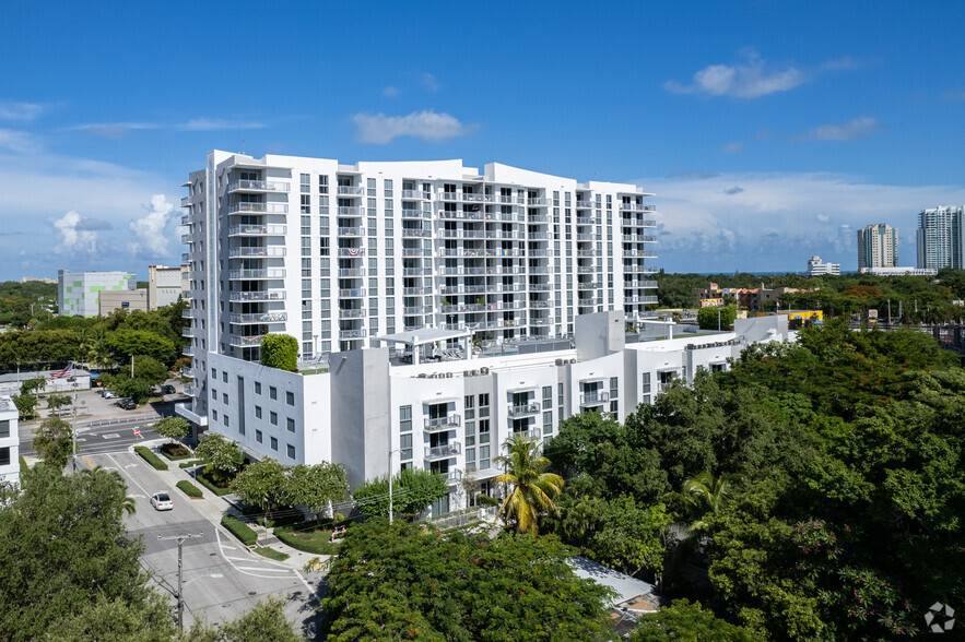 Luxurious high-rise apartment building surrounded by lush greenery under a clear blue sky.