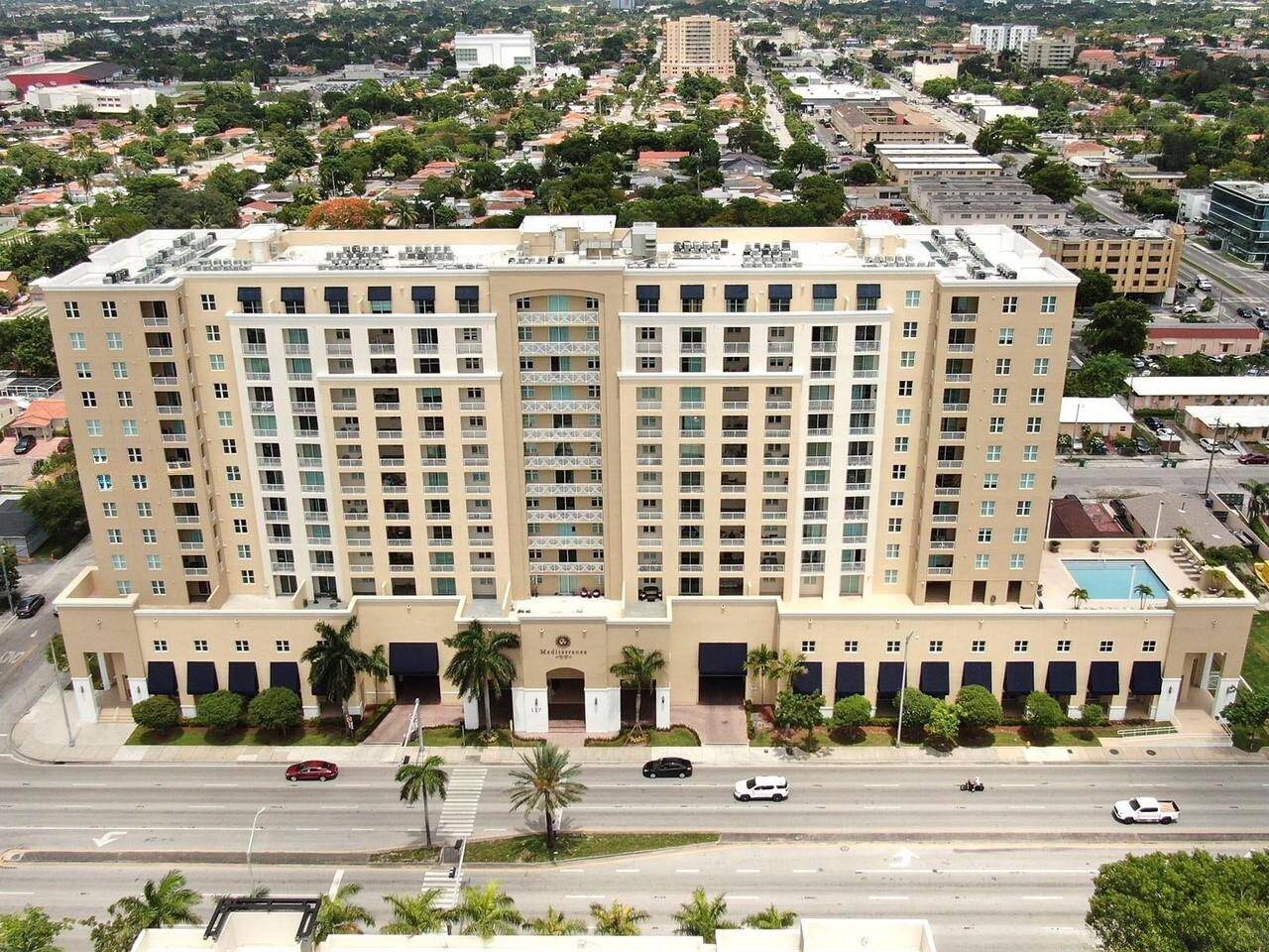 Aerial view of a large residential building with palm trees and a surrounding urban landscape.