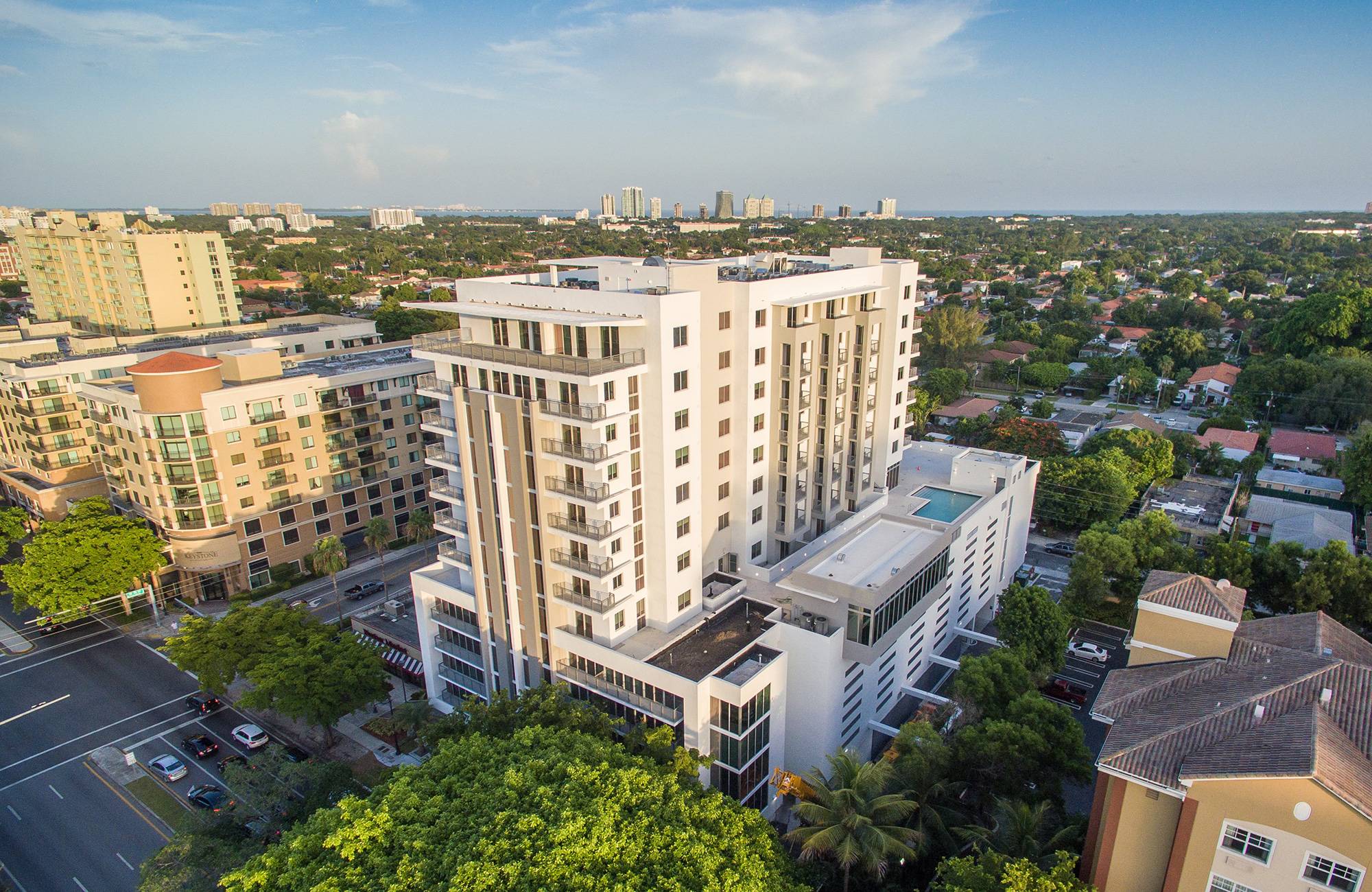 Aerial view of a modern high-rise building surrounded by green trees and cityscape.