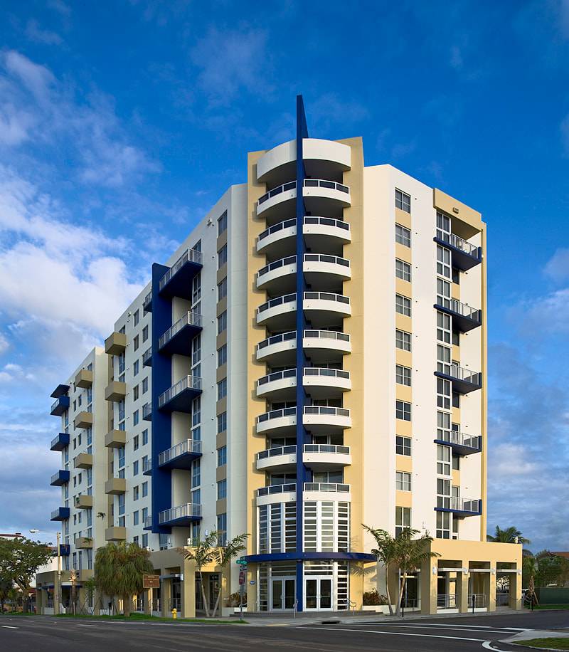 Modern high-rise apartment building with balconies and blue accents under a vibrant sky.