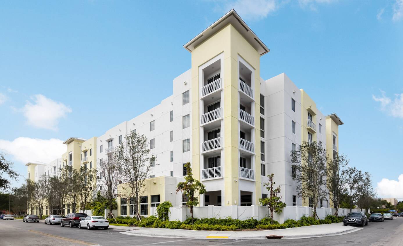Modern five-story residential building with balconies and lush greenery.