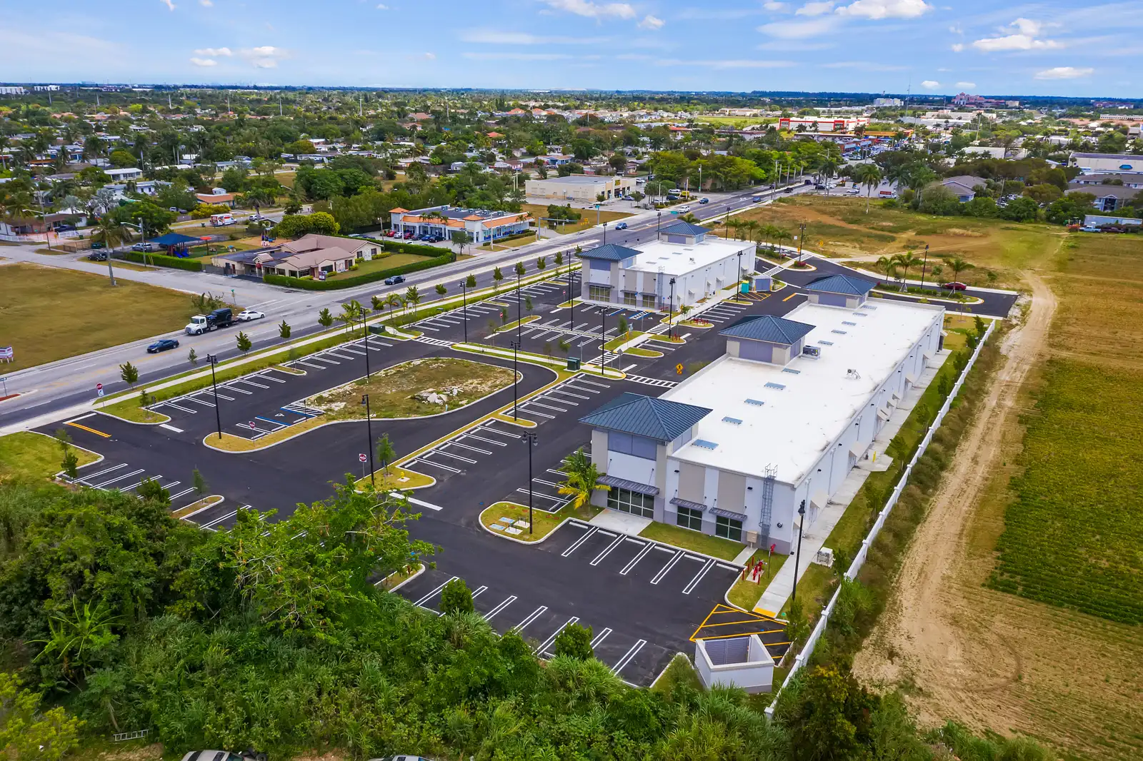 Aerial view of a modern building complex surrounded by a spacious parking area and lush greenery.