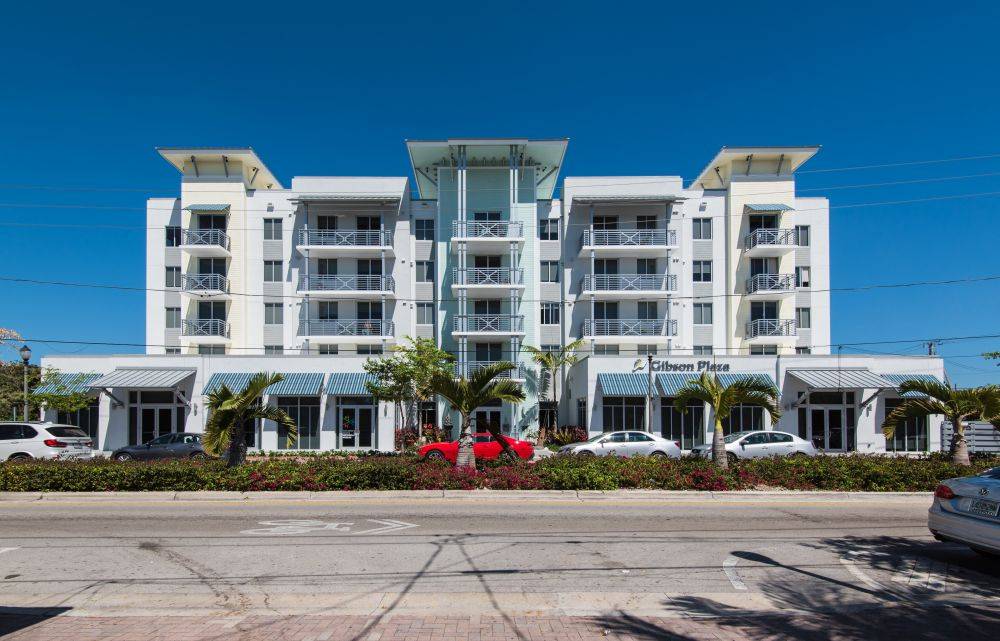 Modern white and glass apartment building with palm trees lining the front, under a clear blue sky.