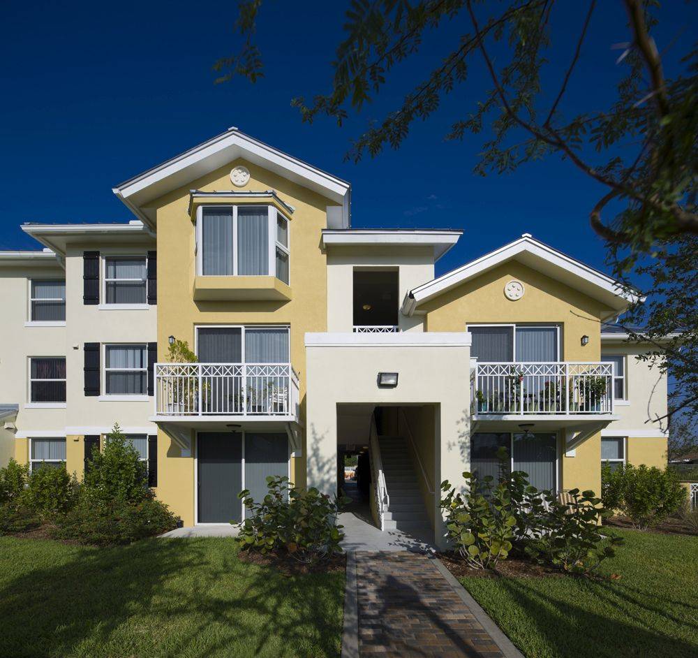 Yellow and white modern apartment building with balconies and lush landscaping.