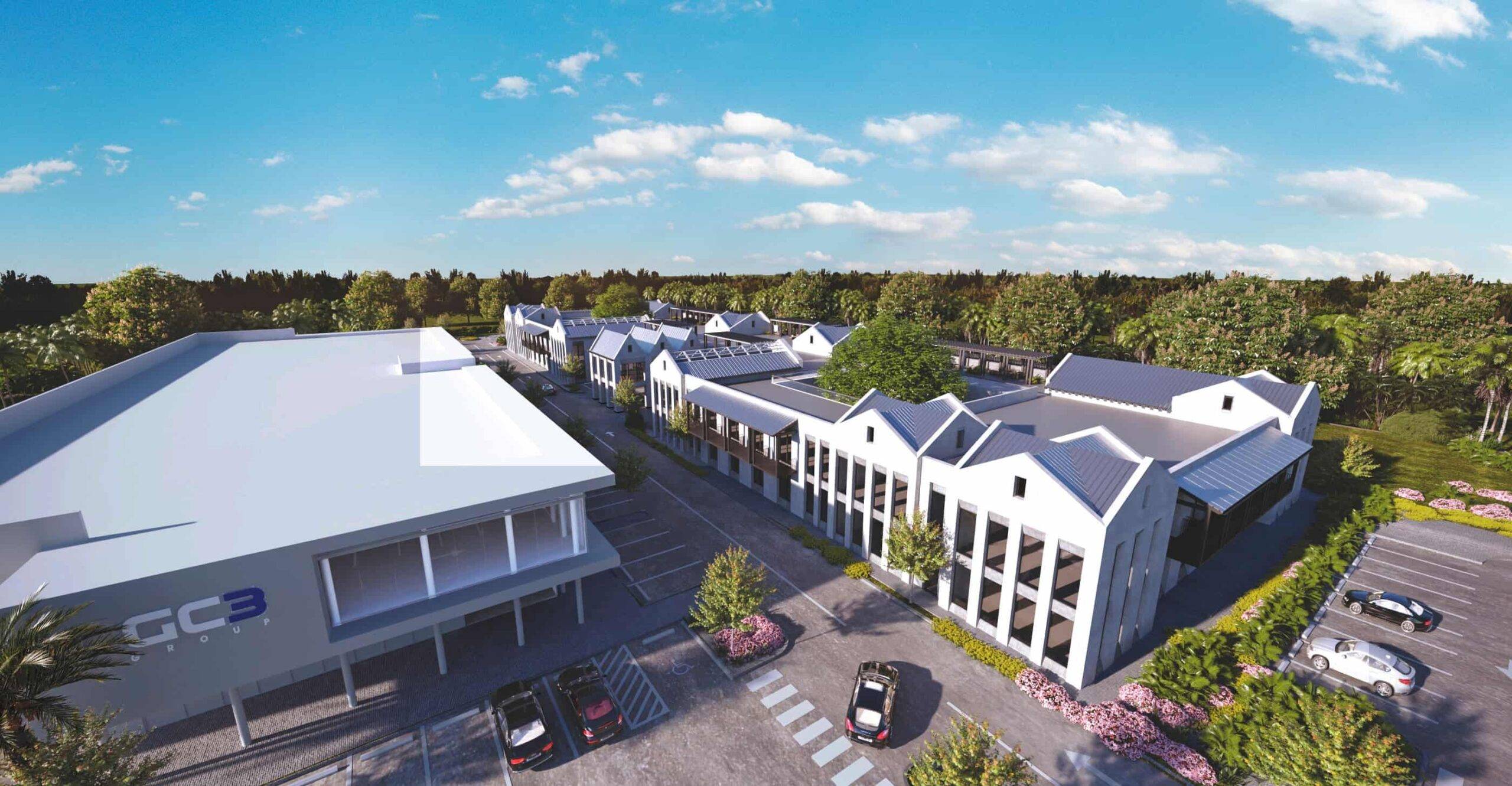 Aerial view of a modern commercial complex with spacious parking, surrounded by lush greenery under a clear blue sky.