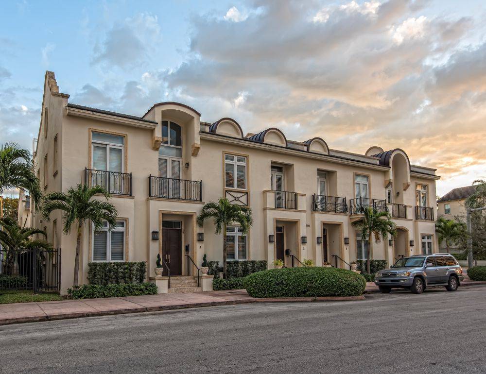 Elegant townhouses with palm trees and a car at sunset