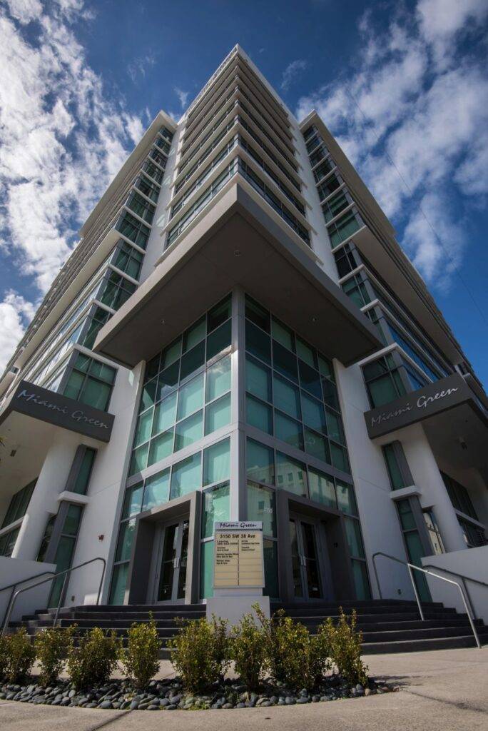 Modern high-rise building with green glass windows under a vibrant blue sky.