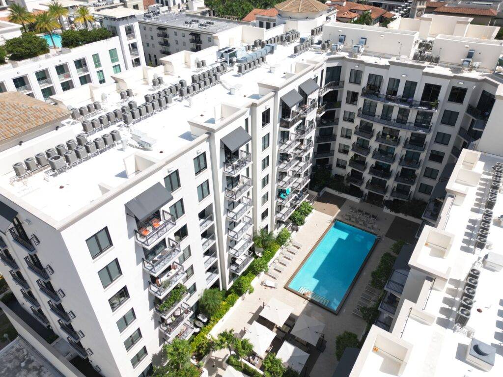 Aerial view of a modern apartment complex with a central pool and lush greenery.