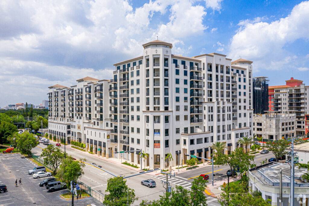 Aerial view of a modern multi-story apartment building under a cloudy blue sky.