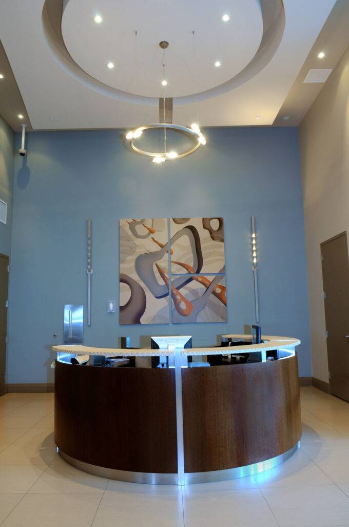 Modern reception desk under elegant lighting with abstract art on a blue wall.