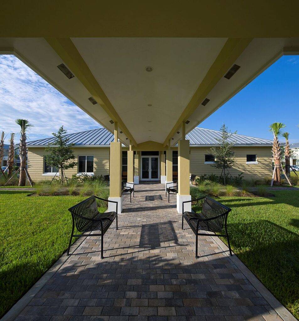Modern house entryway with lush greenery and palm trees under a covered walkway.