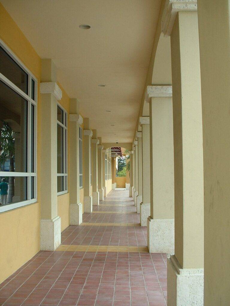 Elegant architectural walkway with columns and tiled floor, leading towards an open courtyard.
