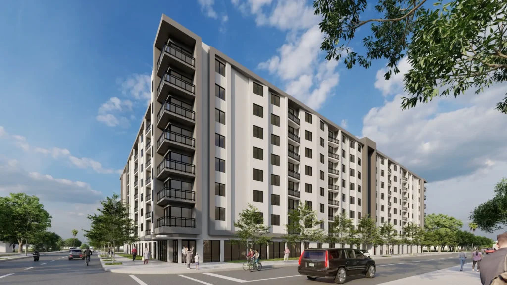 Modern multi-story apartment building with balconies and trees lining the street under a blue sky.
