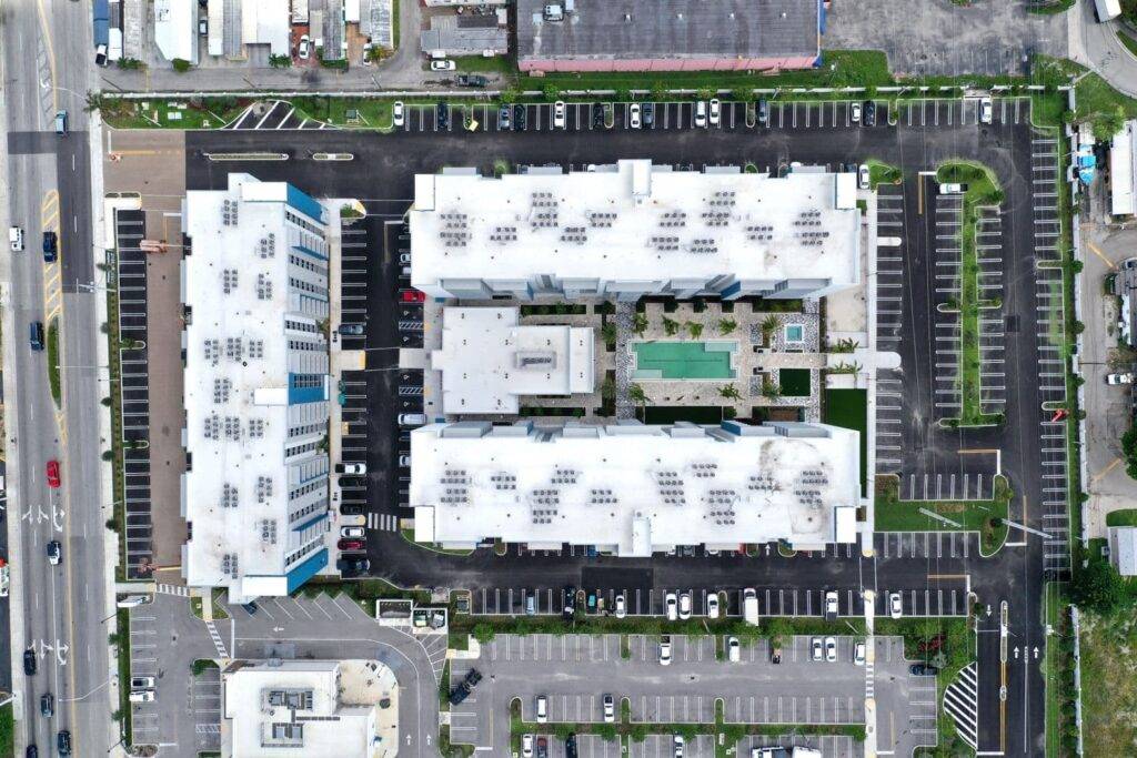 Aerial view of a modern urban complex with two white-roofed buildings, central courtyard, and swimming pool.