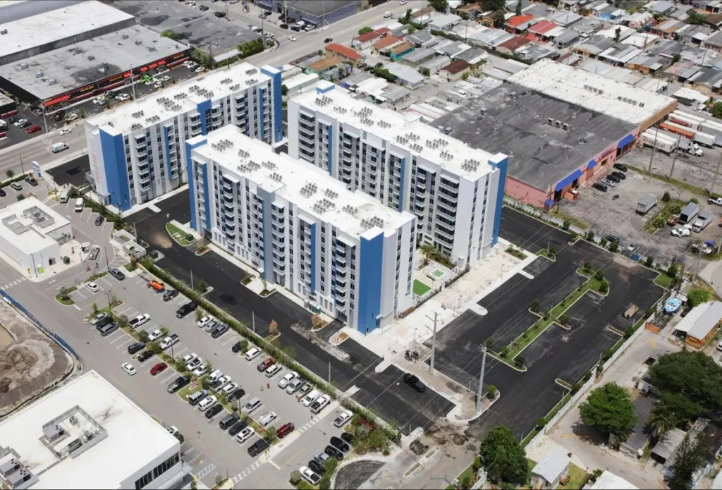 Aerial view of modern apartment complex with blue accents surrounded by parking and greenery.