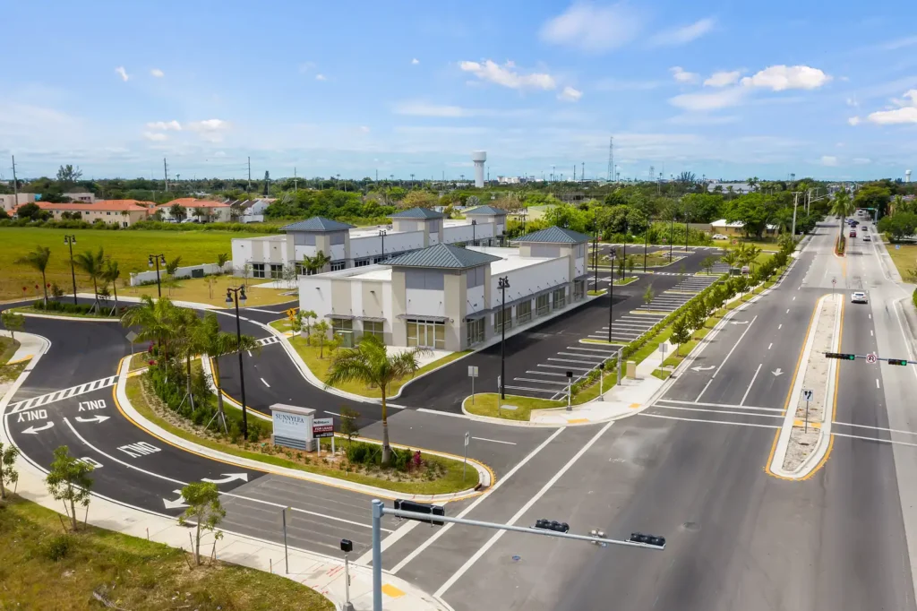 Modern commercial building with landscaped surroundings and ample parking on a sunny day.