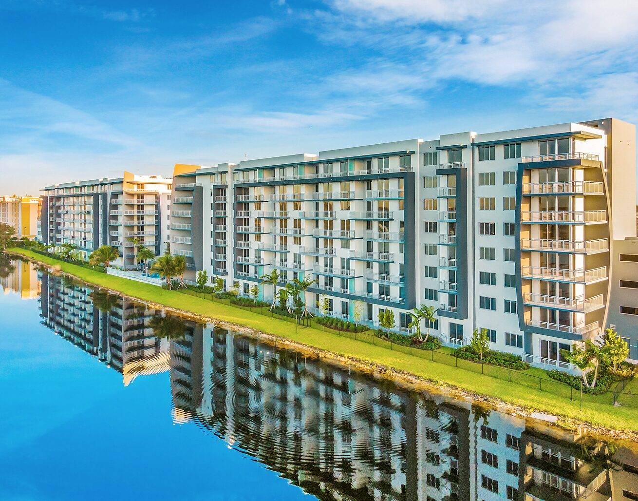 Modern waterfront apartment buildings with a clear blue sky reflected in a calm canal.