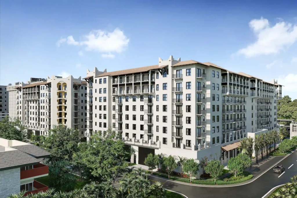 Modern multi-story apartment complex with green landscaping and blue sky.