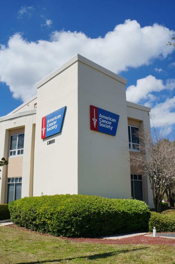 American Cancer Society Hope Lodge building under a blue sky with lush green bushes in the foreground.