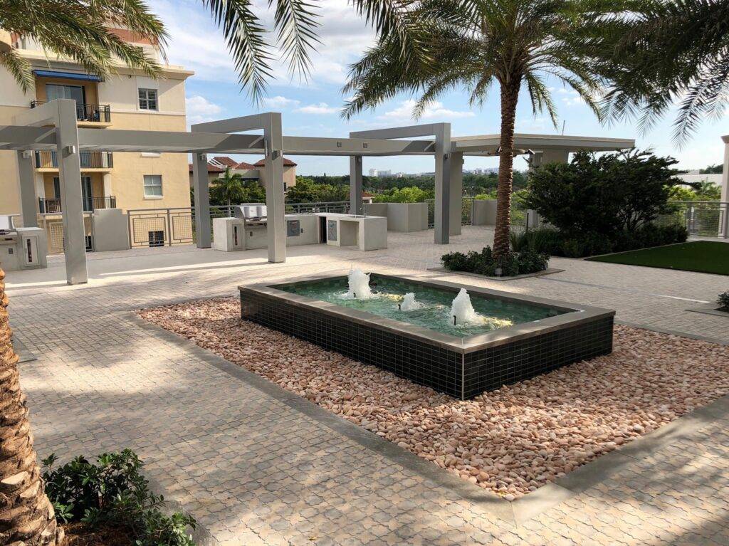Modern courtyard with a sleek fountain flanked by palm trees and contemporary architecture.