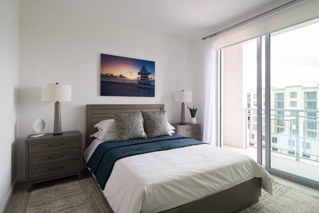 Modern bedroom with stylish decor, featuring a cozy bed, corner lamps, and a serene balcony view.