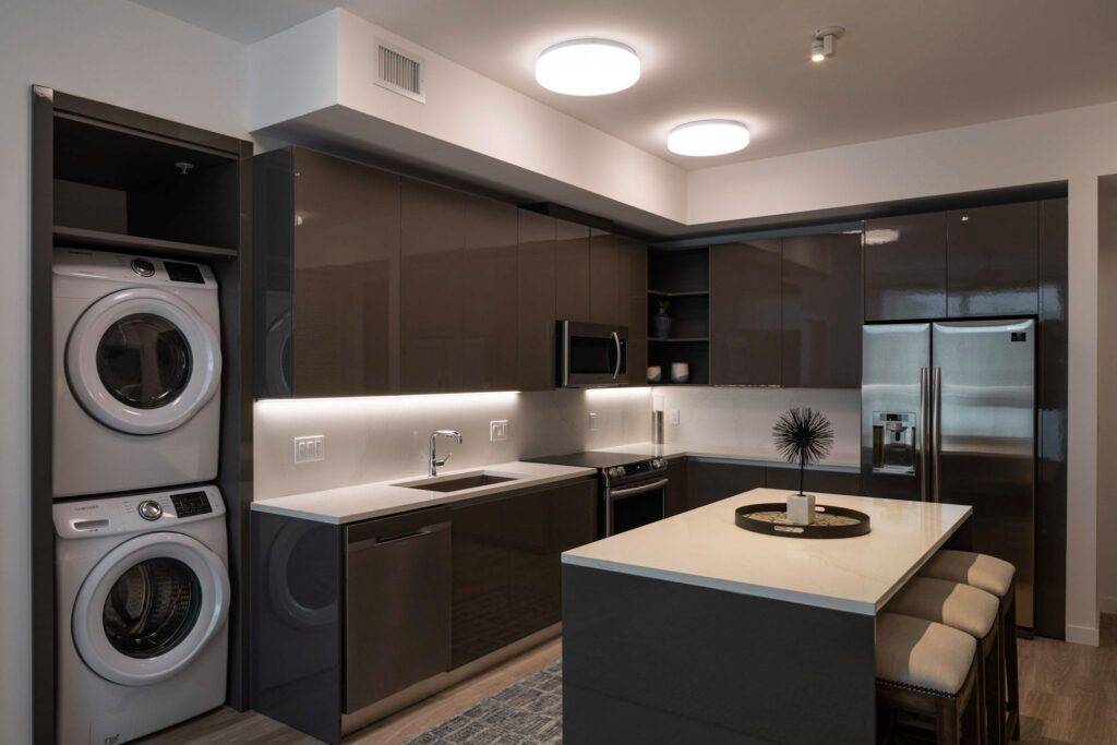 Modern kitchen with sleek dark cabinets, island seating, and laundry appliances integrated.