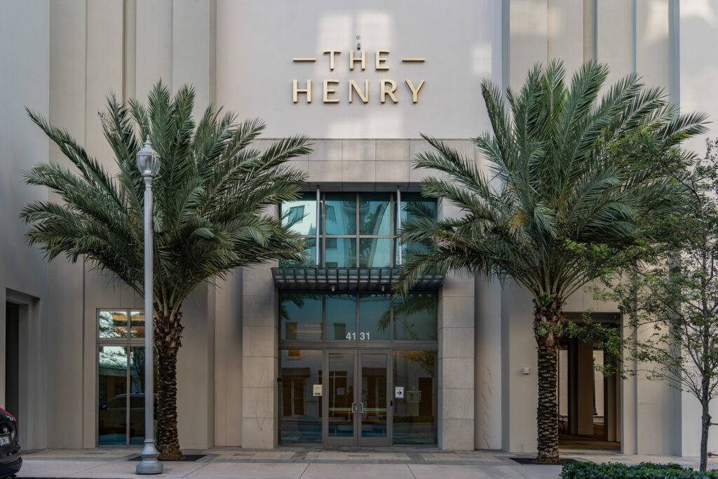 Elegant entrance to The Henry building framed by palm trees.