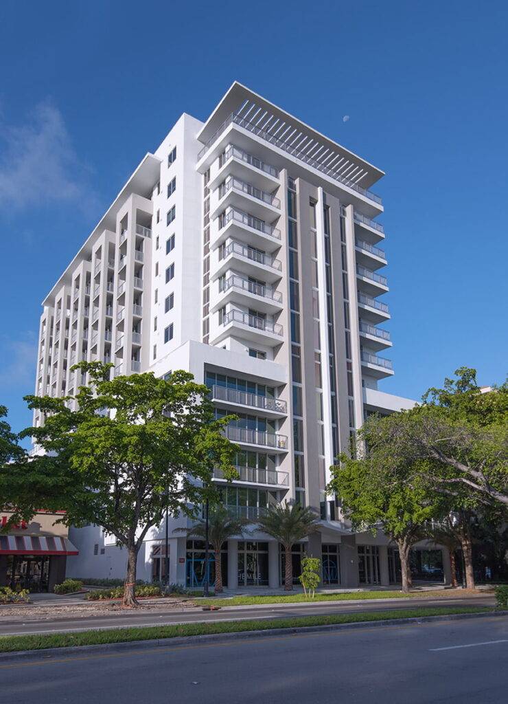 Modern high-rise apartment building under a clear blue sky with surrounding trees.