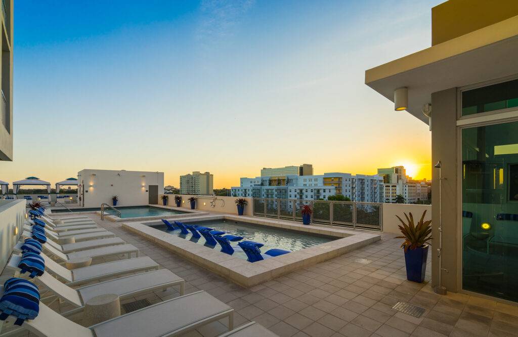 Rooftop pool area with lounge chairs against a cityscape at sunset.