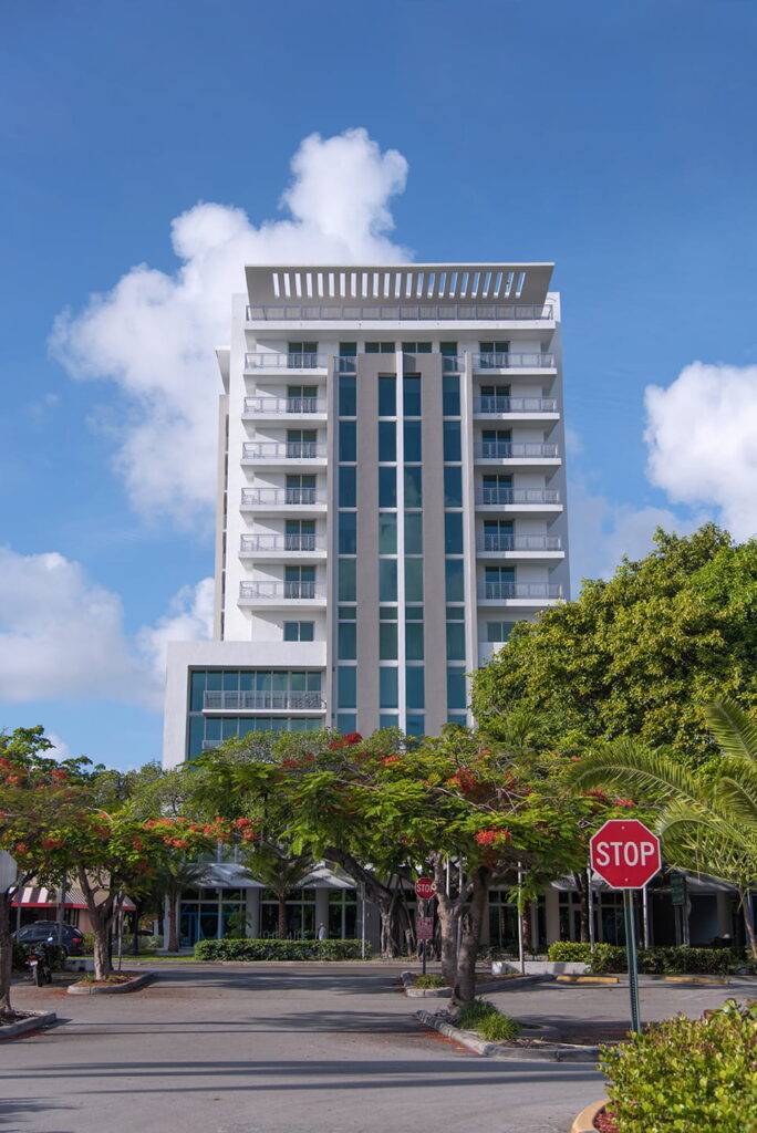 Modern high-rise building with a sleek design surrounded by lush greenery under a bright blue sky.