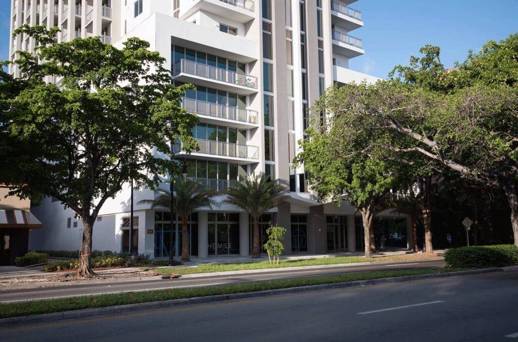 Modern building with glass facade framed by lush green trees on a clear day.