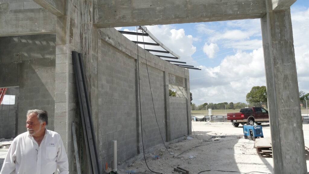 Man in construction site with partially built concrete structure under a blue sky.