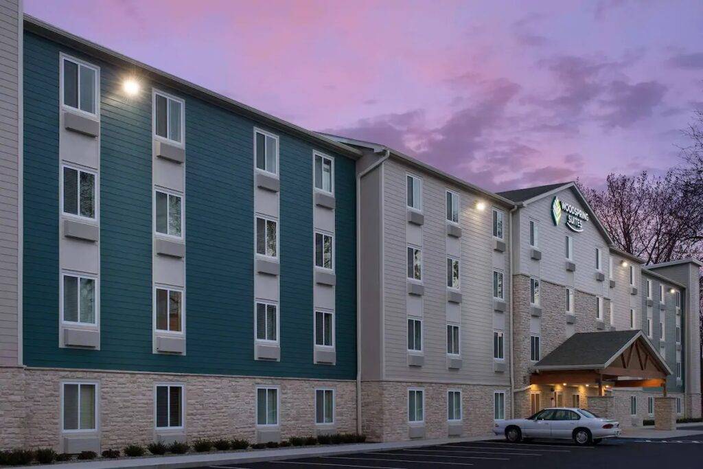 Woodspring Suites hotel exterior at dusk with illuminated windows and a parked car.