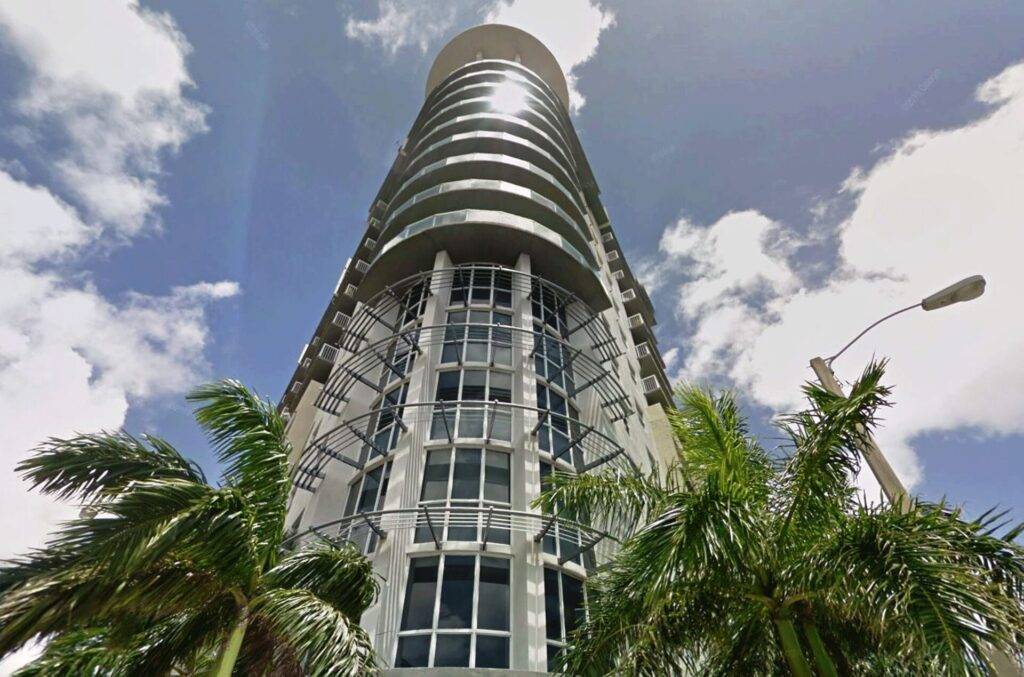 Modern high-rise building in Miami with palm trees and a vibrant blue sky.