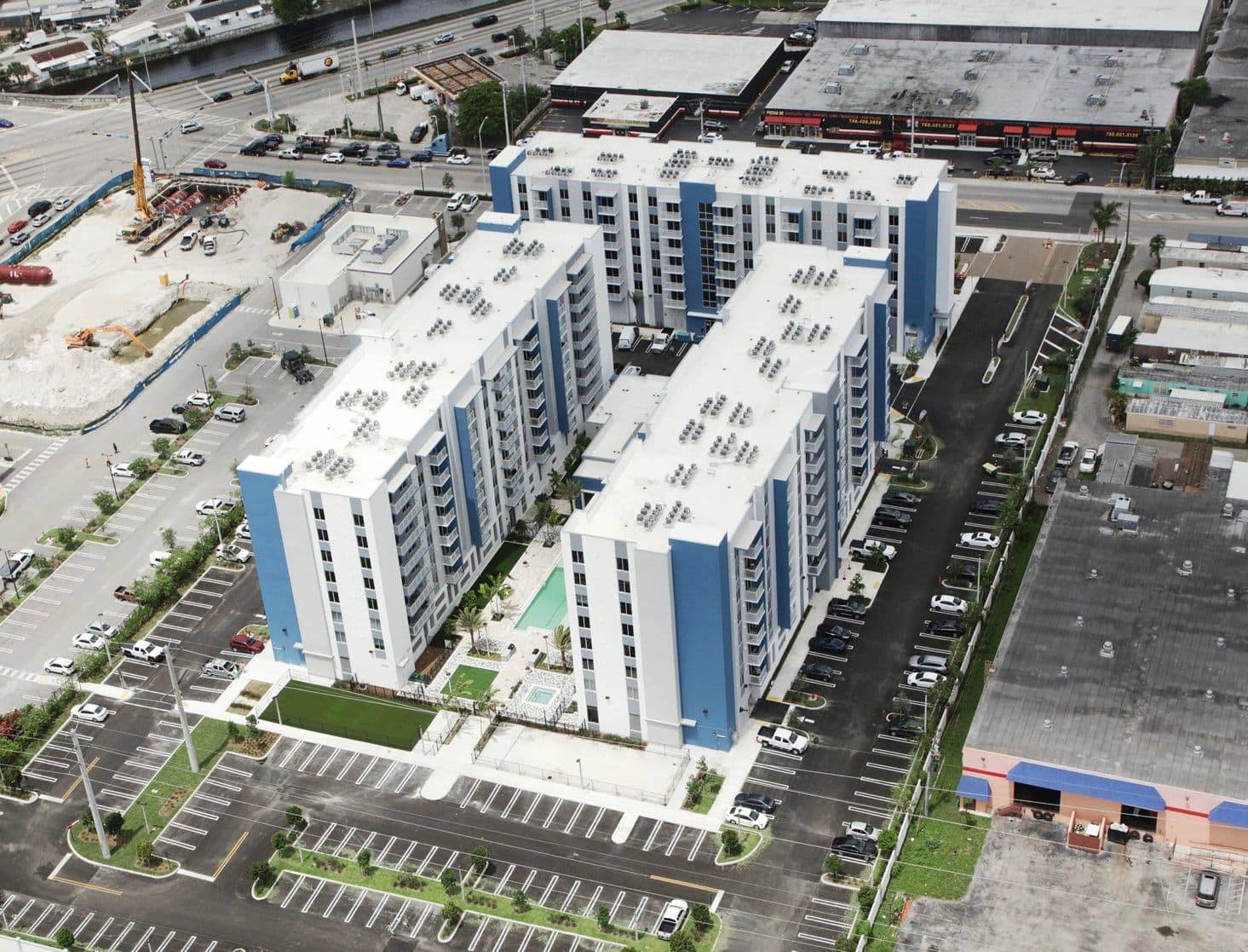 Aerial view of modern residential apartment complex with blue accents and parking area.