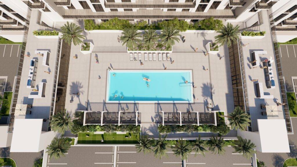 Aerial view of a modern outdoor swimming pool surrounded by palm trees and lounge chairs at a residential complex.