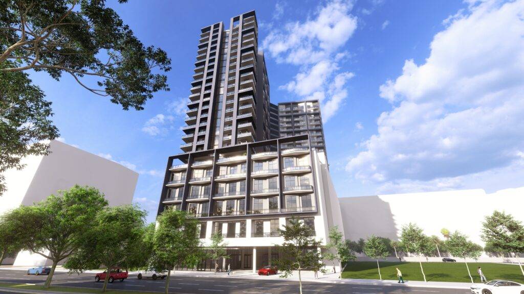 Modern high-rise building with glass facade under a clear blue sky, surrounded by trees and urban landscape.