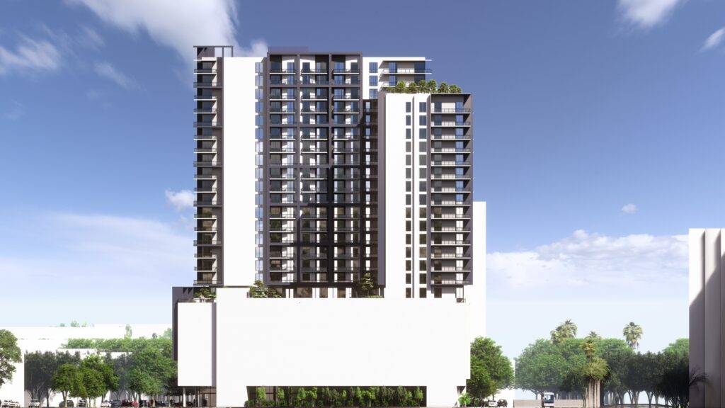 Modern high-rise building against a clear blue sky with lush green surroundings.