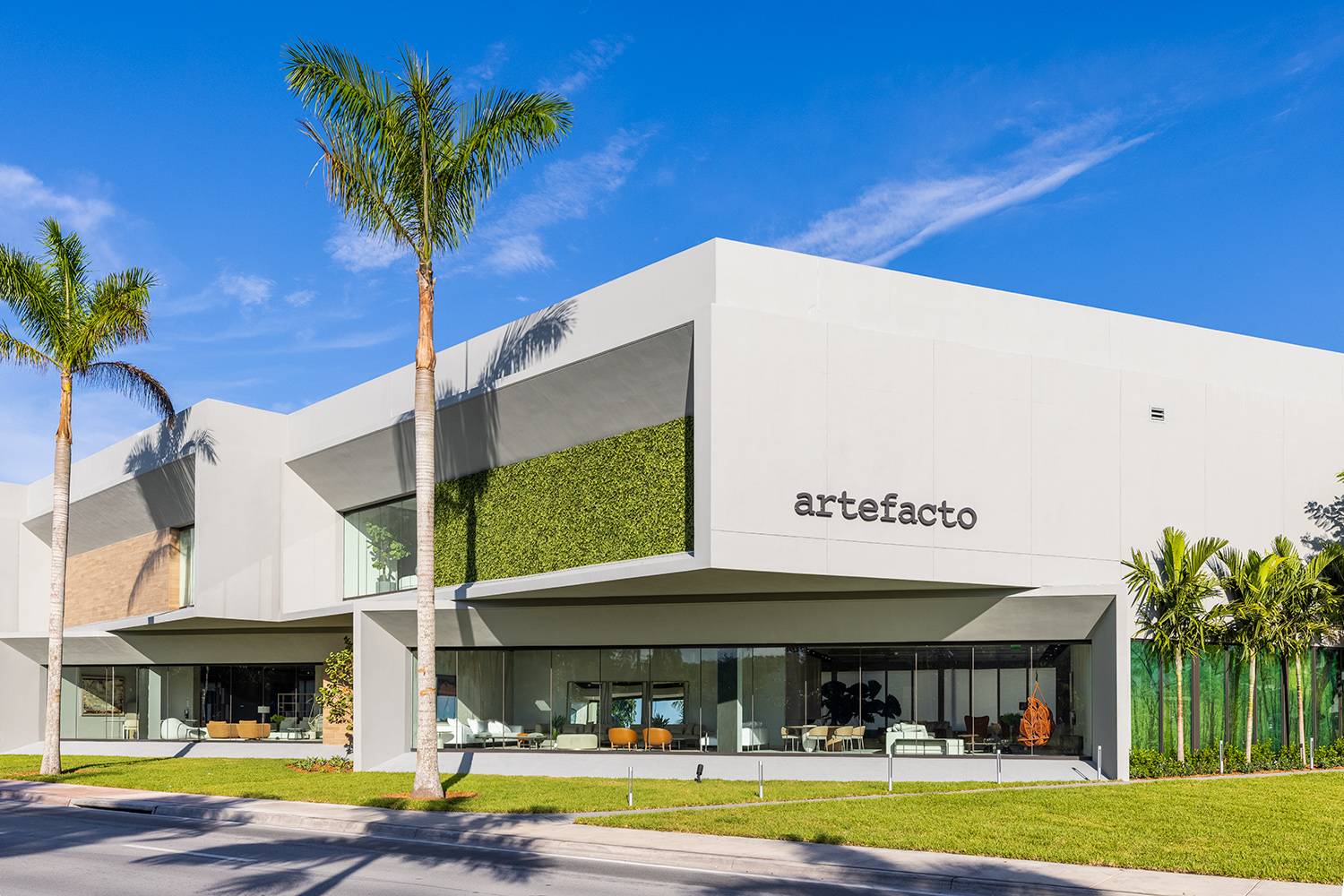 Modern facade of the Artefacto Coral Gables showroom with palm trees and blue sky.