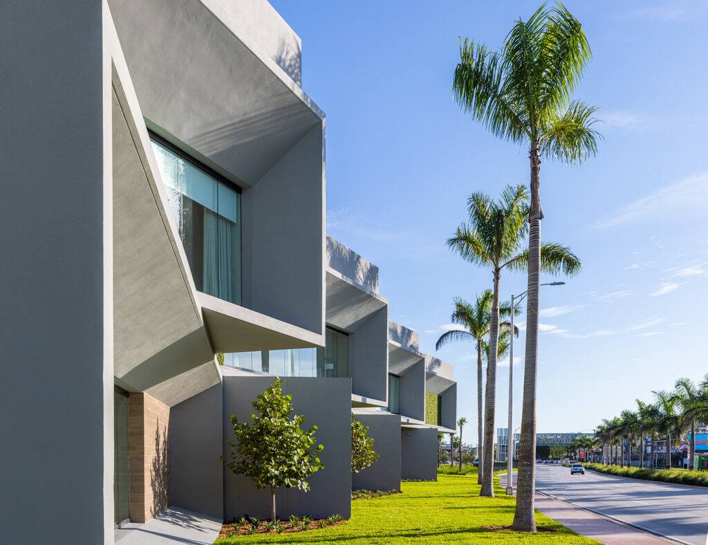 Modern architectural building with angular design and tall palm trees under a clear blue sky.