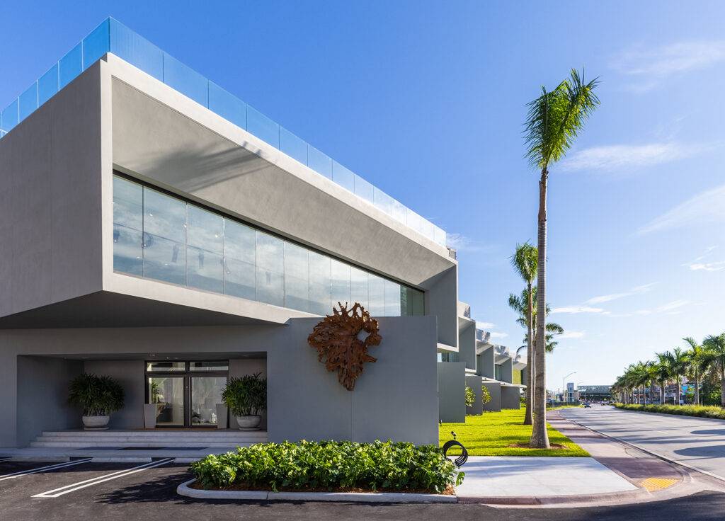 Modern architectural design of a sleek showroom with lush greenery and palm trees under a bright blue sky.
