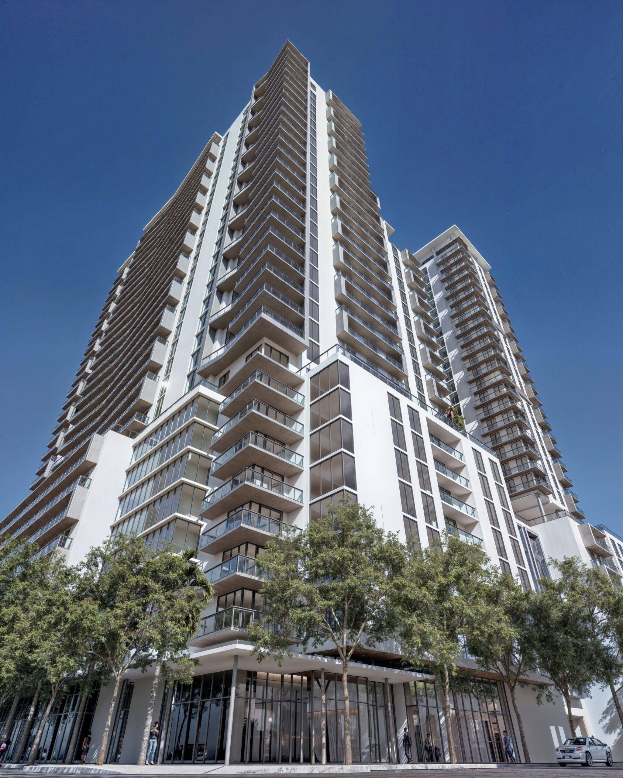 Modern high-rise building with glass balconies against a clear blue sky.