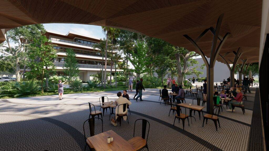 Outdoor seating area with tables and chairs under a canopy, surrounded by lush greenery and people relaxing.